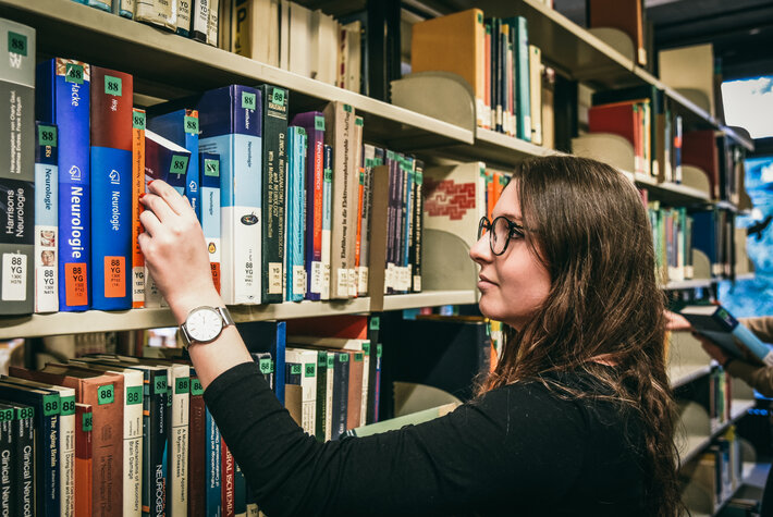 Eine junge Frau wählt an einem Bücherregal im Lesesaal Biologie der Universität Regensburg ein Buch aus. (öffnet Vergrößerung des Bildes)