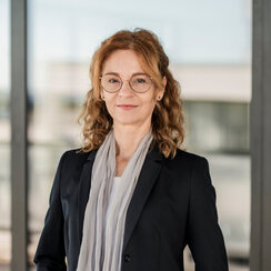 Eine Frau mit Brille und langen dunkelblonden Haaren blickt lächelnd in die Kamera.