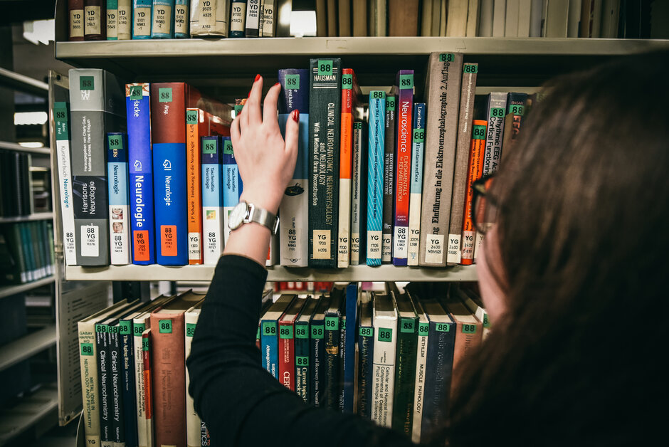 Eine Frau greift nach einem Buch in einem Bücherregal