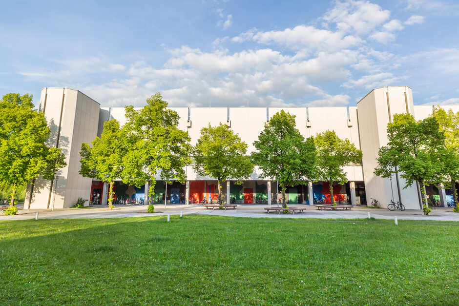 Blick über eine Wiese und Bäume auf den Gebäudeteil Philosophie/Theologie am Campus der Universität Regensburg