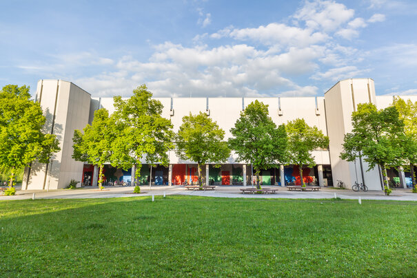 Blick über eine Wiese und Bäume auf den Gebäudeteil Philosophie/Theologie am Campus der Universität Regensburg