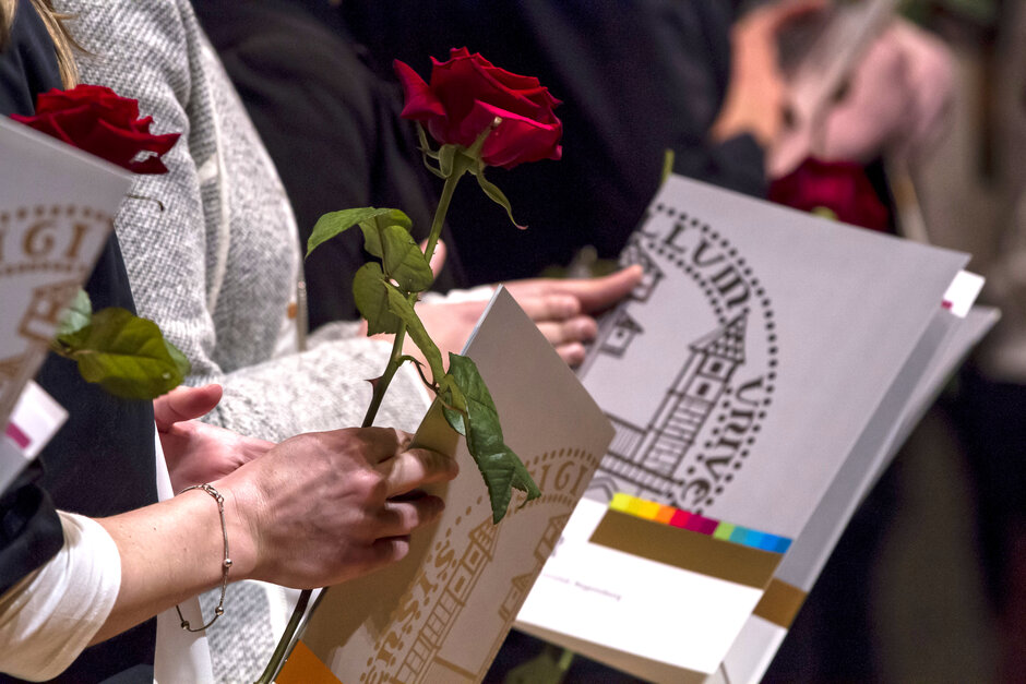 Absolventenfeier: Studierende halten Urkundenmappen im Design der Universität Regensburg und langstielige rote Rosen in den Händen.
