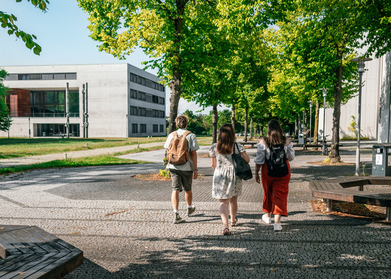 Eine Gruppe Studierender geht auf das Vielberth-Gebäude am Campus der Universität Regensburg zu.