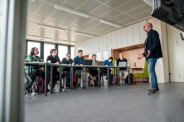 Ein Dozent hält einen Vortrag vor einer Gruppe von Studierenden in einem modern ausgestatteten Seminarraum an der Universität Regensburg